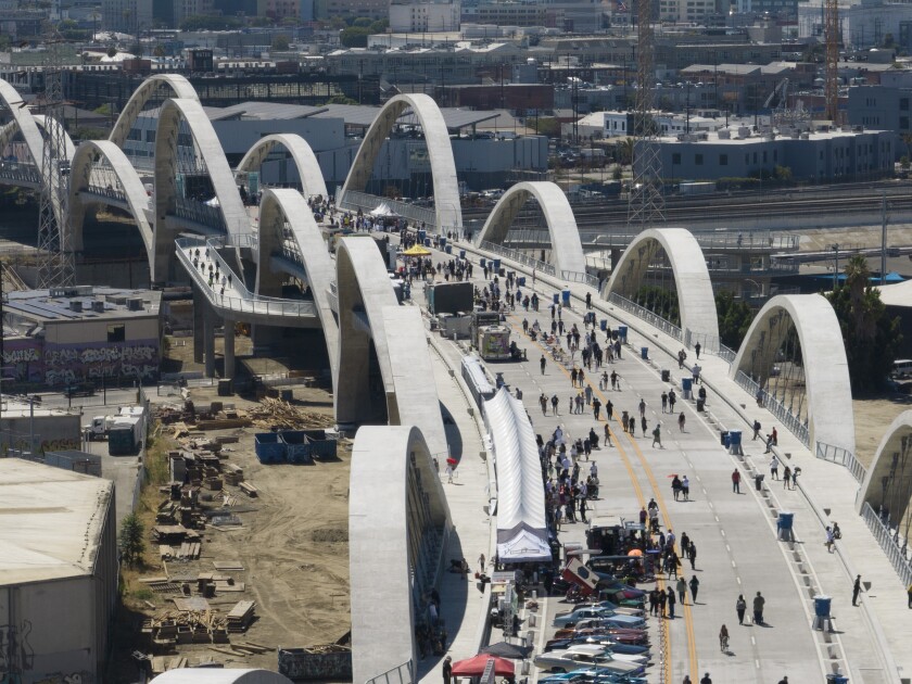 An overhead view of a bridge bordered by arches and filled with pedestrians, tents and cars. 
