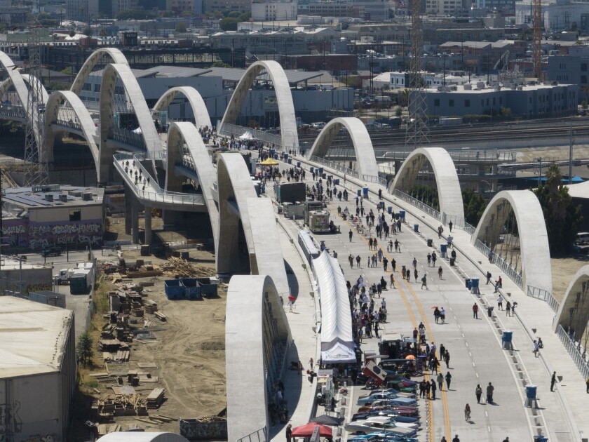 An overhead view of a bridge bordered by arches and filled with pedestrians, tents and cars.