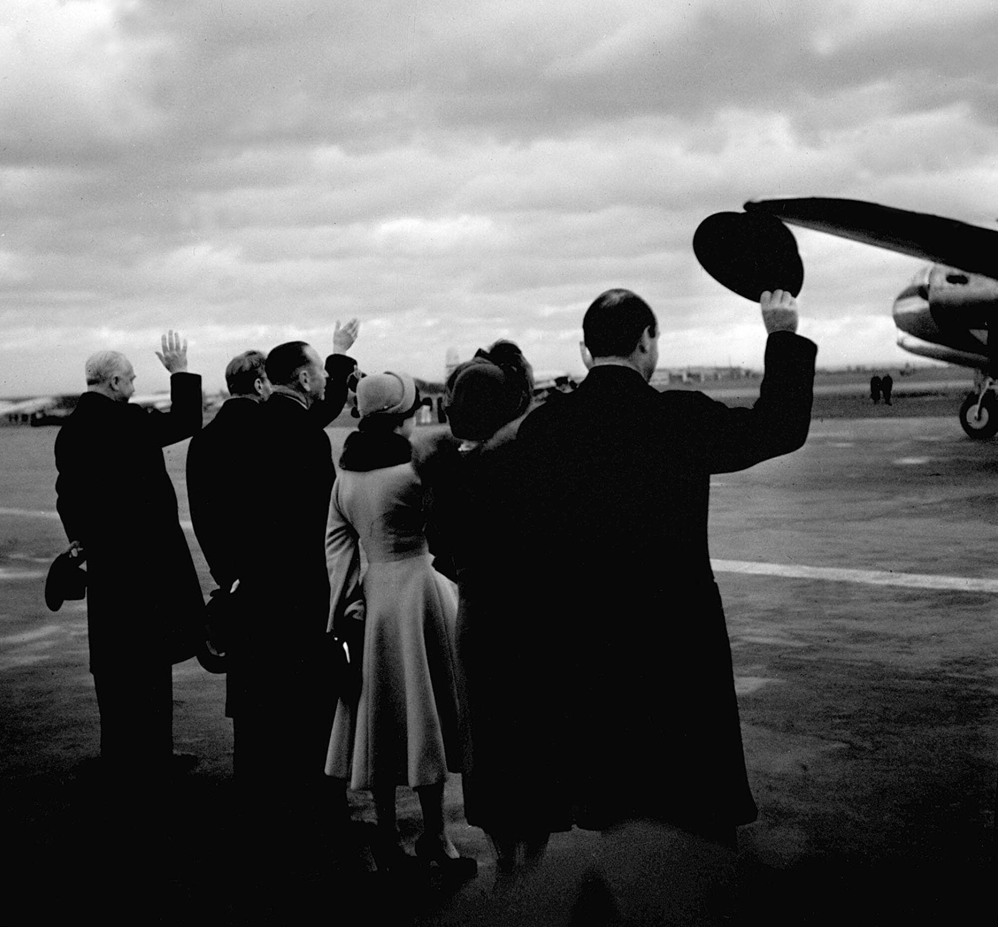 A group of men and women wave as they stand near a plane 