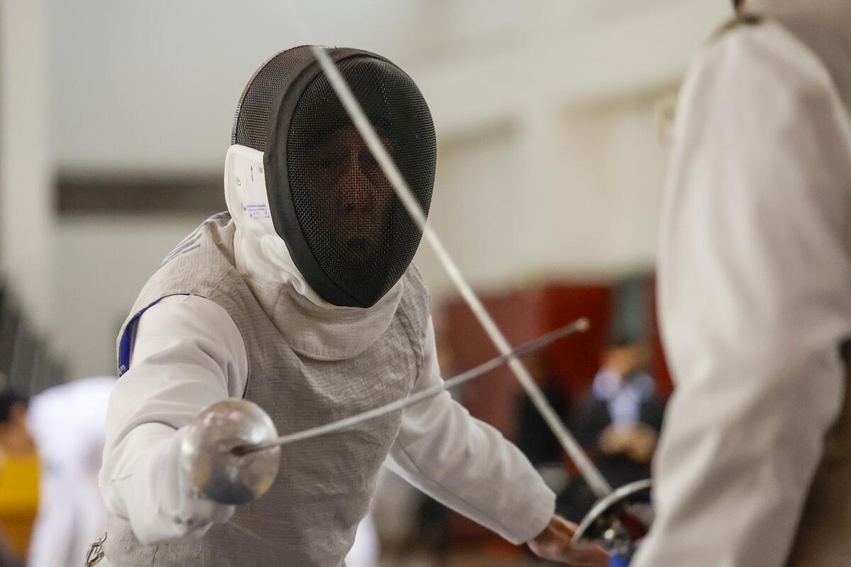 A man wearing a fencing mask points a thin sword at his opponent.