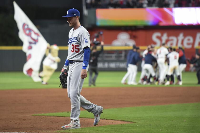 Atlanta, GA - October 16: Los Angeles Dodgers first baseman Cody Bellinger, left, walks off the field as the Atlanta Braves celebrate a walk-off RBI single by Austin Riley to end game one in the 2021 National League Championship Series at Truist Park on Saturday, Oct. 16, 2021 in Atlanta, GA. The Braves won 3-2. (Wally Skalij / Los Angeles Times)