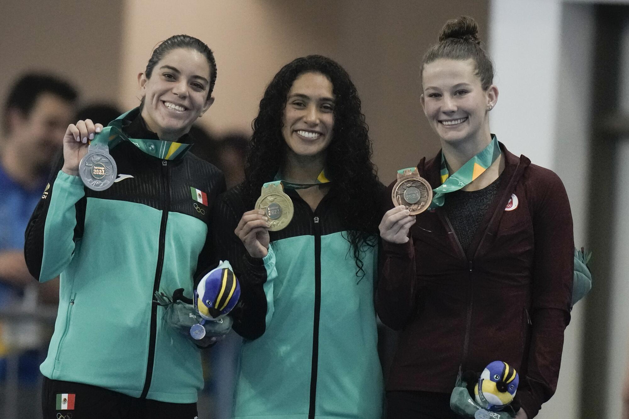 Gaby Agundez, center, holds her gold medal while standing next to silver medalist Alejandra Orozco, left, and Caeli Mckay.