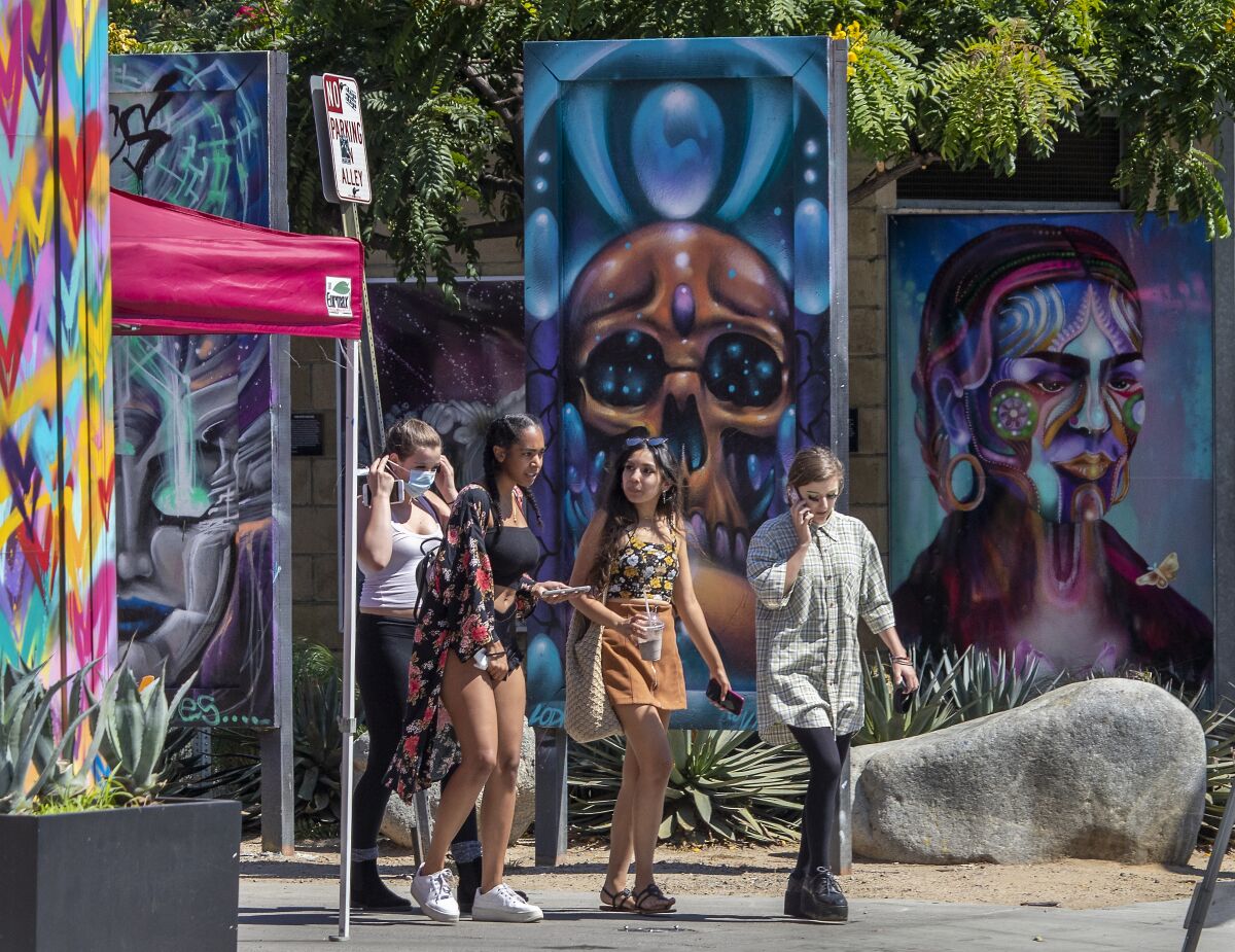 A pedestrian wears a mask while others don't while walking past Munchies Vegan Deli and murals near 4th Street in Santa Ana.
