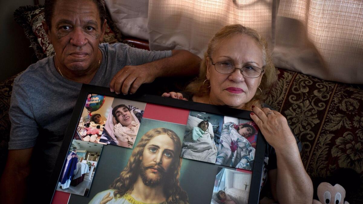 Juan Manuel González y María González Muñoz posan, el 4 de septiembre, en San Juan con un retrato de Jesús y fotos de su hermana Ramona, quien falleció a los 59 años de una septicemia.