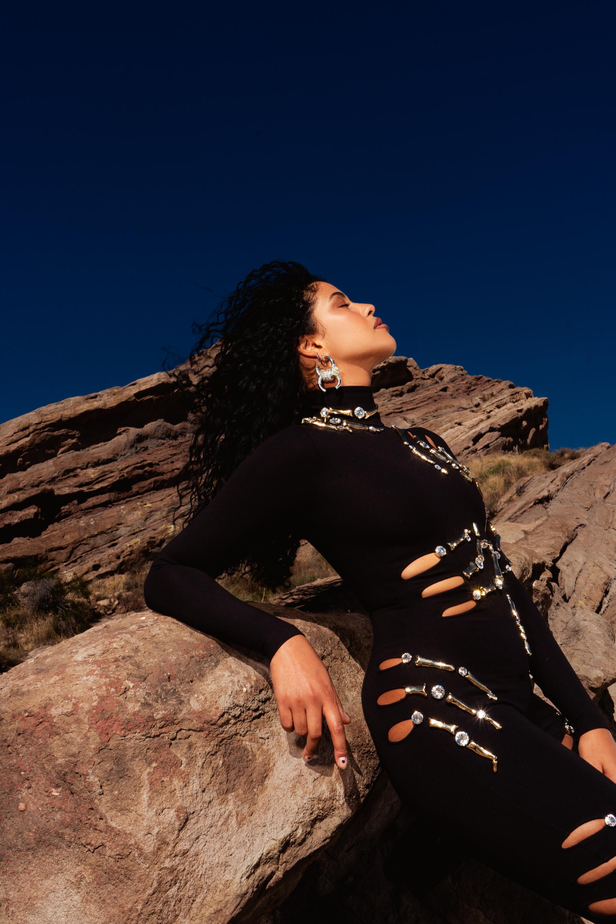 The artist Yendry poses in an all black outfit in the desert.