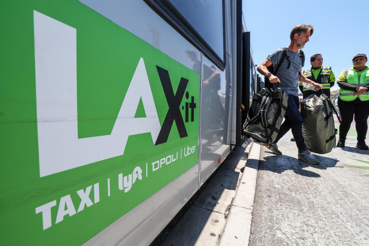 A person carrying suitcases steps off a bus with a LAX-it sign on its side