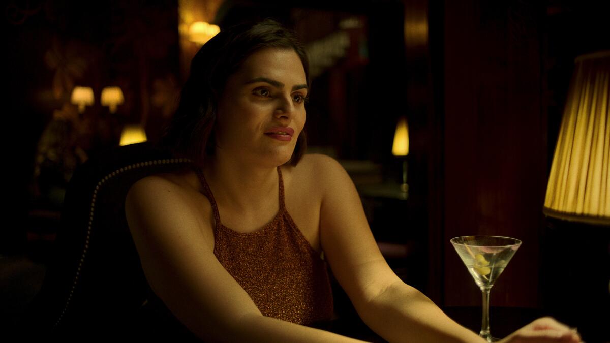 A woman in a red blouse sitting with a martini glass in front of her.