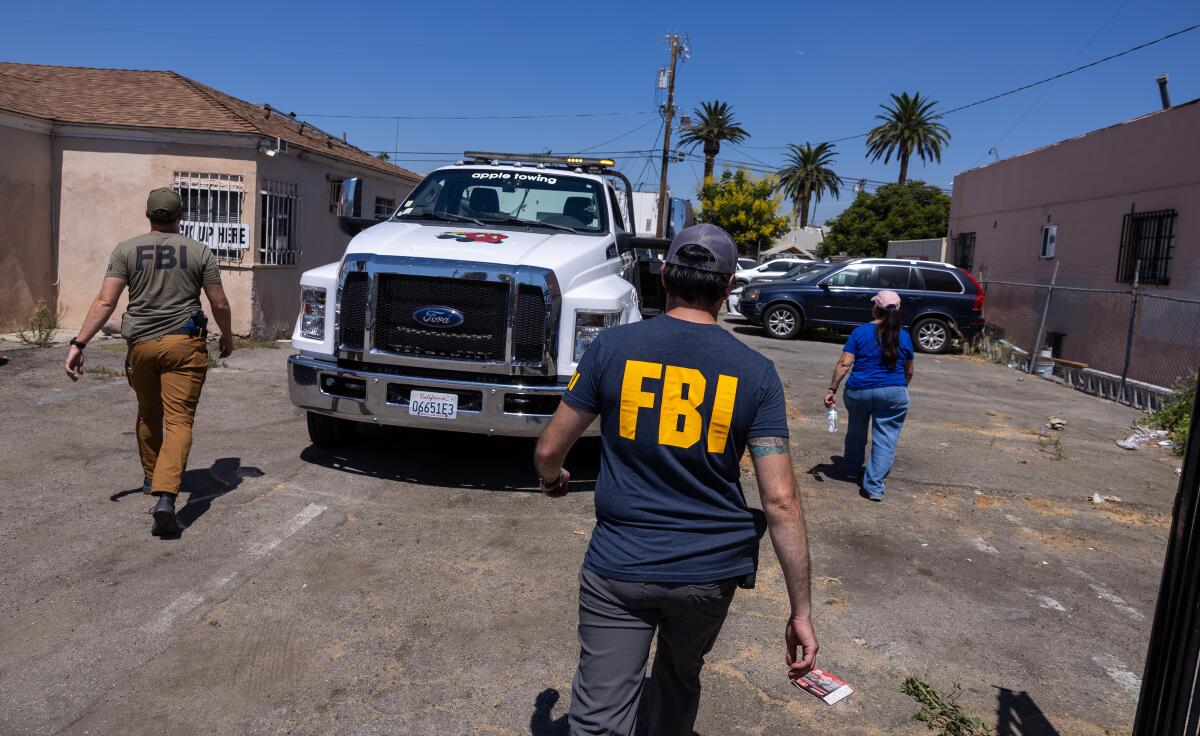 Two people in T-shirts labeled "FBI" approaching vehicles in a parking lot