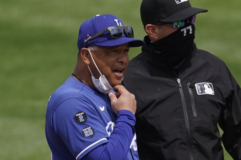 Los Angeles Dodgers manager Dave Roberts, left, chats with umpire Jim Reynolds (77) before a spring training baseball game.
