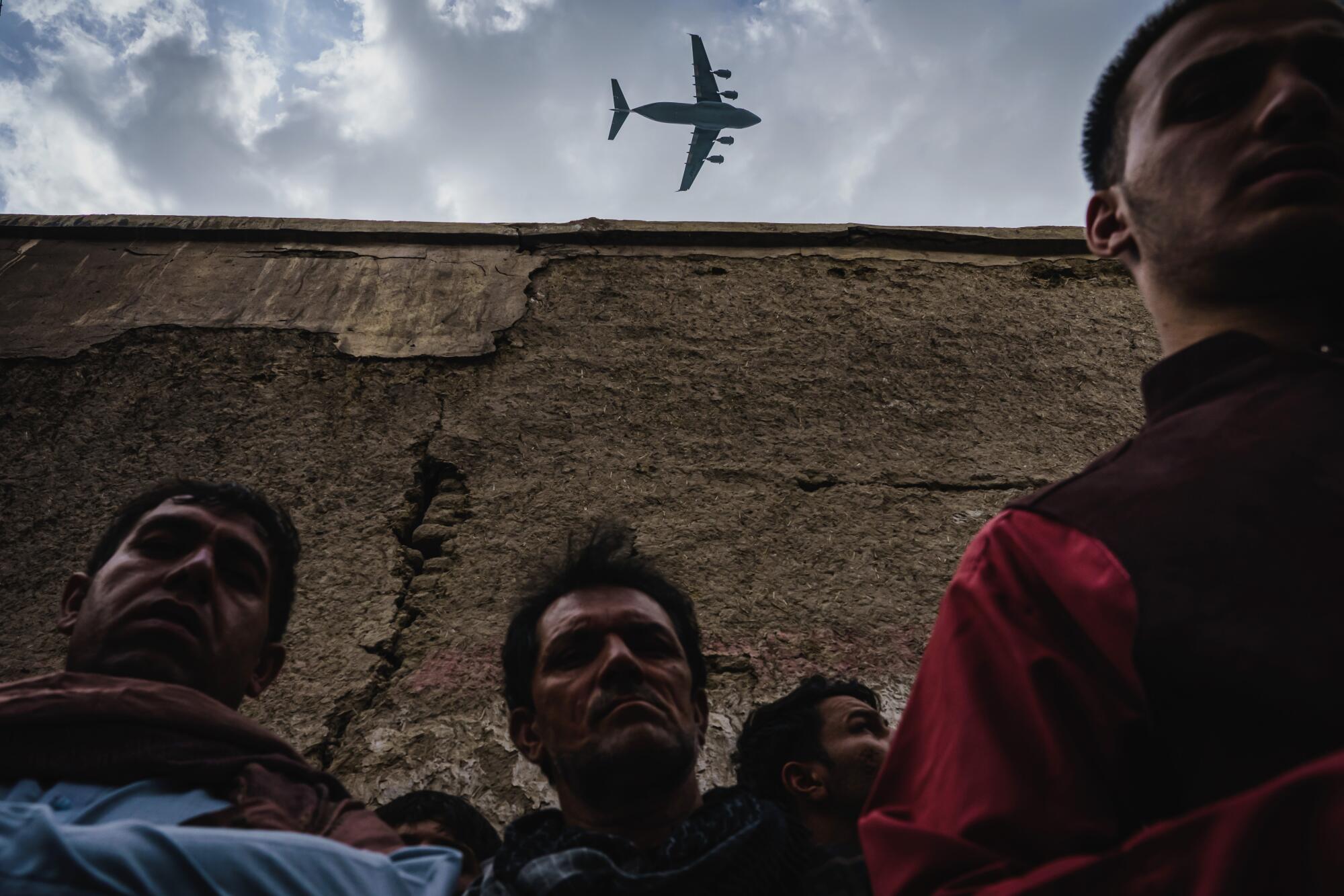 A military transport plane flies over an Afghan family