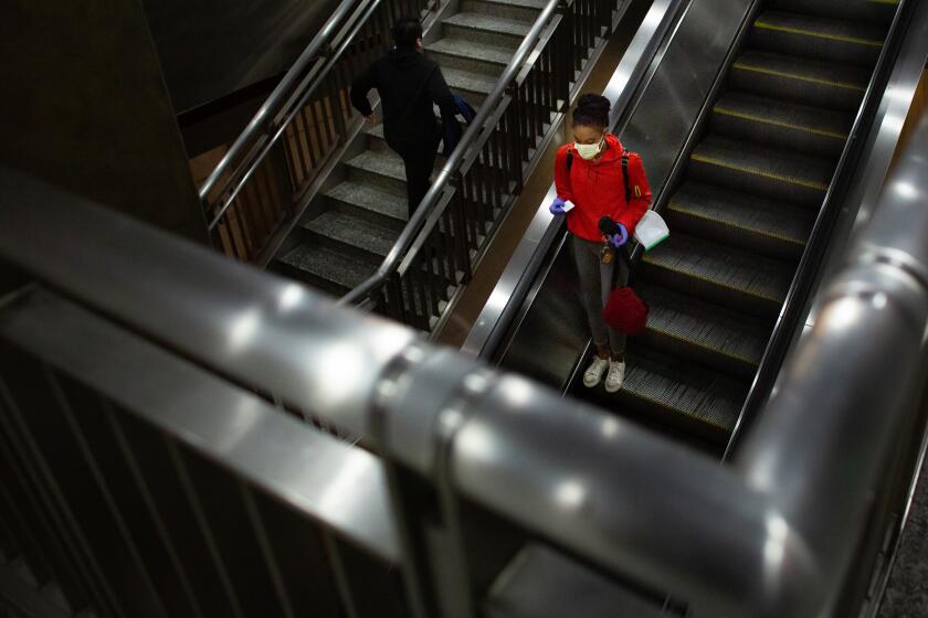 LOS ANGELES, CA - MARCH 26: A woman wearing a mask rides the escalator in the Hollywood/Highland Metro Station during the coronavirus pandemic on Thursday, March 26, 2020 in Los Angeles, CA. (Jason Armond / Los Angeles Times)