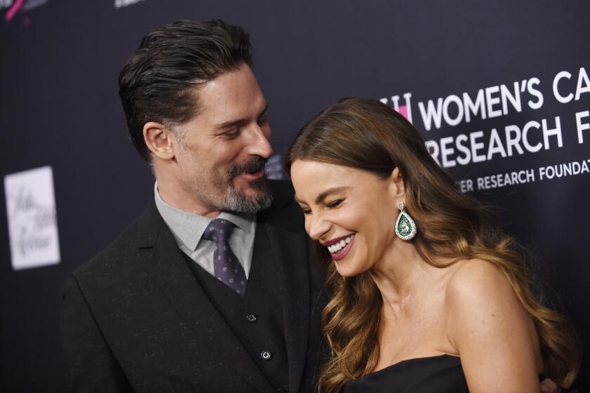 Sofia Vergara in a black dress and Joe Manganiello in a black suit are laughing together while posing for photos