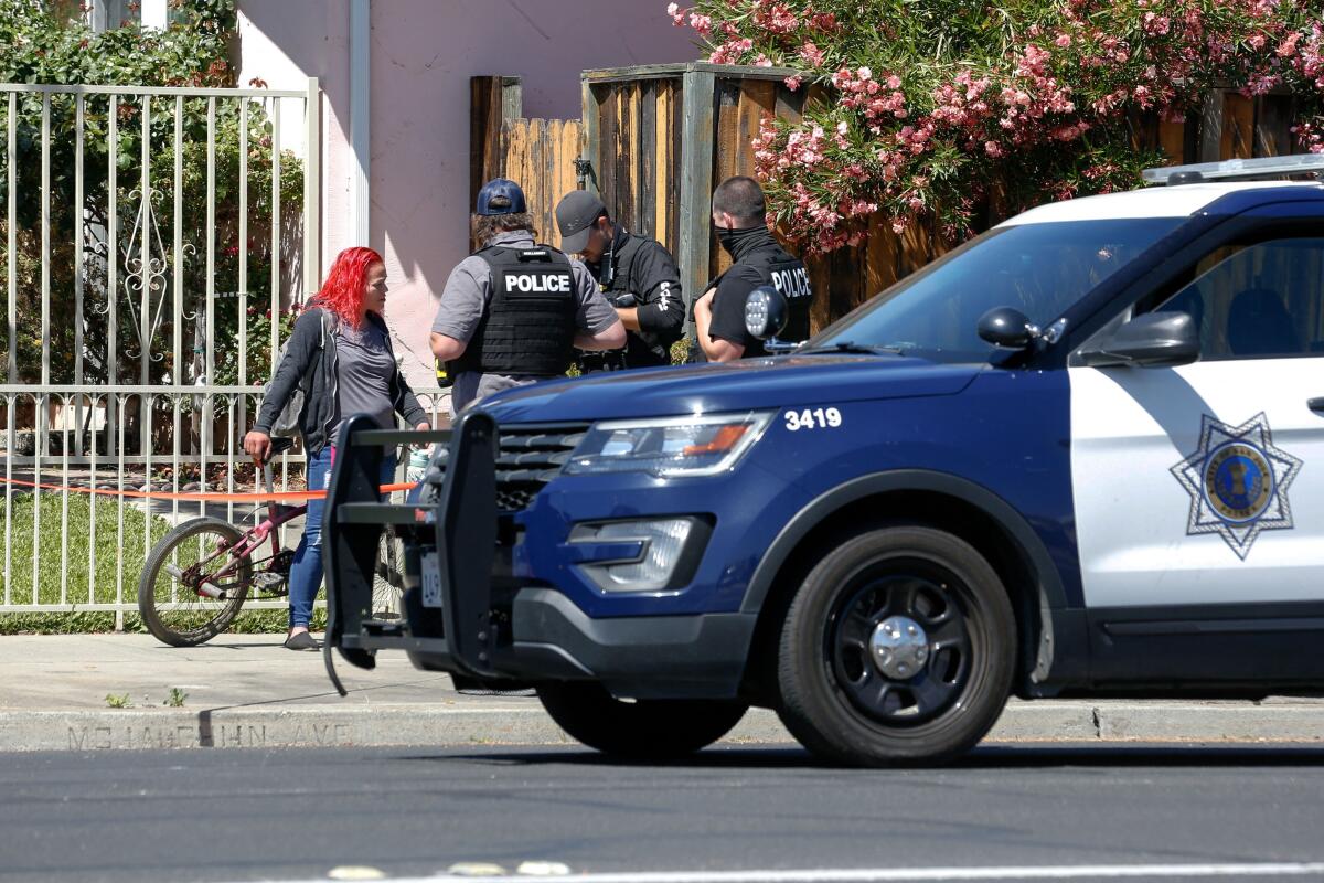 San Jose police officers stand on a sidewalk near a police vehicle talking to a person with red hair.