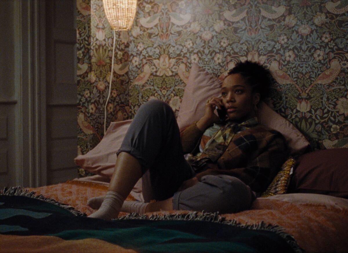 A woman lays on her bed talking on the phone, a floral wallpaper wall behind her