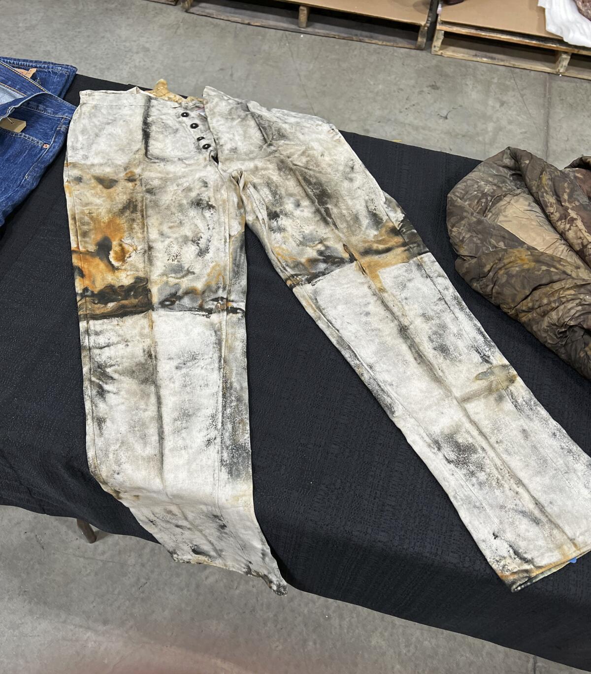 A pair of old, distressed work pants salvaged from a shipwreck lie on a table