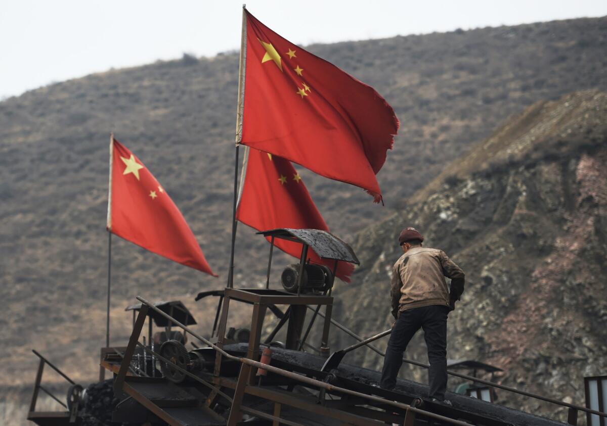 Chinese flags fly as a worker clears a conveyer belt near a coal mine at Datong, in China's northern Shanxi province, on Nov. 20, 2015.