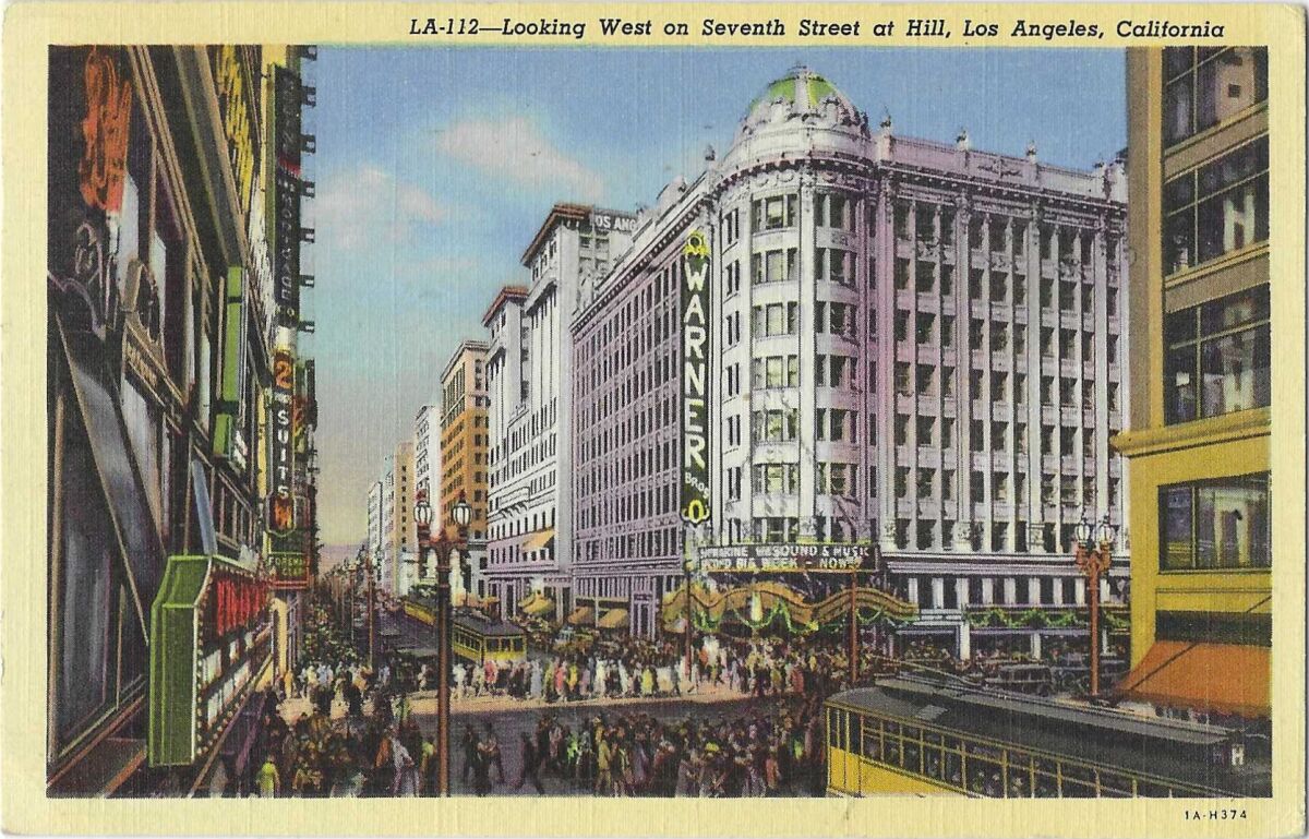 Vintage postcard depicts a daytime street scene, with pedestrians, streetcars and the Warner Bros. theater