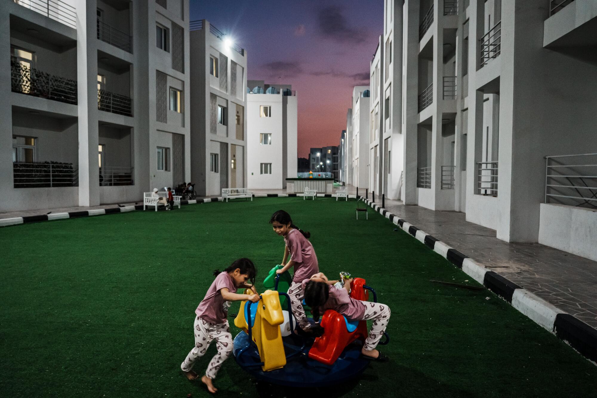 晚上，三个孩子在公寓楼之间的长长的人造草坪上玩耍