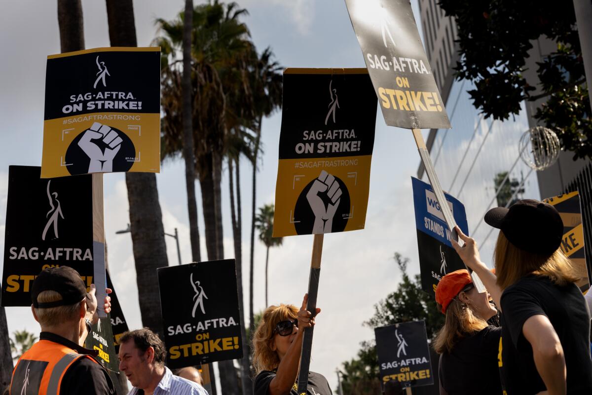 People hoist black-and-yellow picket signs that read, "SAG-AFTRA on Strike."