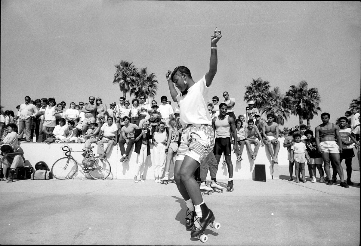 A vintage black and white photo shows a young Black woman skating before a crowd in Venice.