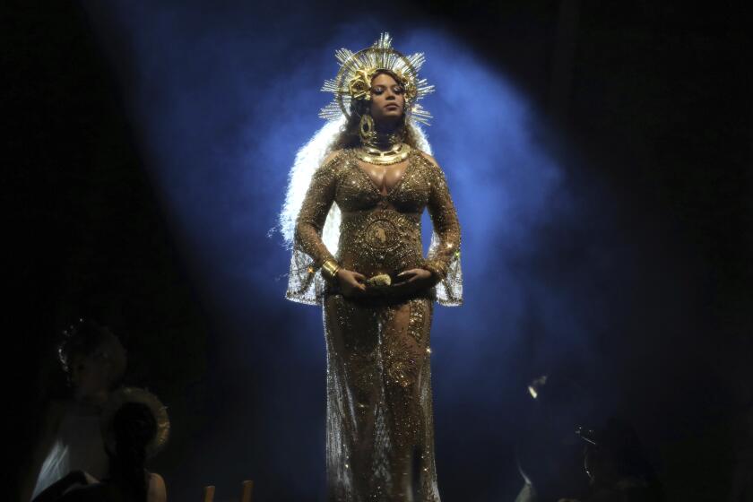 A woman posing on a stage in a sheer gold dress and an elaborate crown