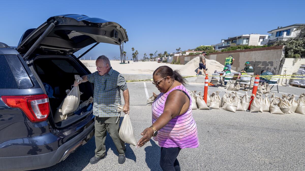 Man and a woman put sand bags in the trunk of their car. 