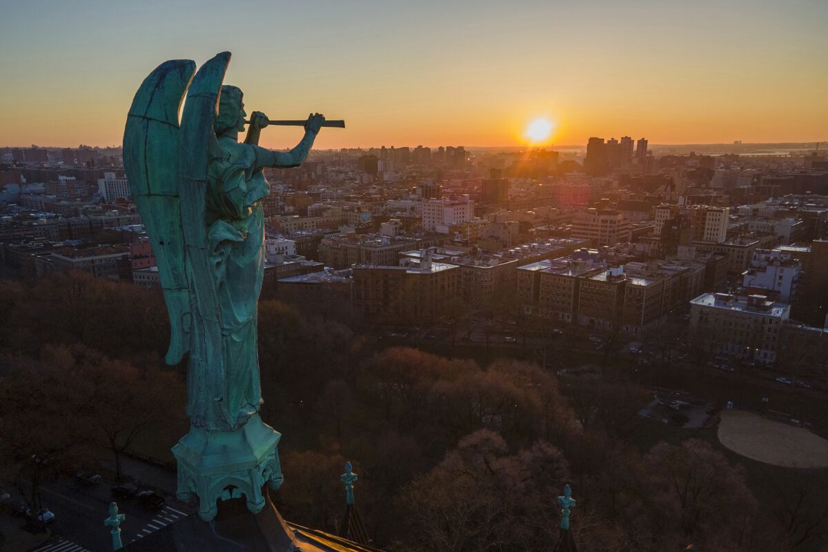 FILE - A bronze statue of the Archangel Gabriel blowing a trumpet stands atop the Cathedral of St. John the Divine as the sun rises in the Morningside Heights neighborhood of the borough of Manhattan in New York City on Sunday, March 26, 2023. The county that encompasses Manhattan added more than 17,000 residents in the year ending last July after losing almost 111,000 people in the previous 12-month period, according to population estimates released Thursday, March 30, 2023, by the U.S. Census Bureau. (AP Photo/Ted Shaffrey, File)