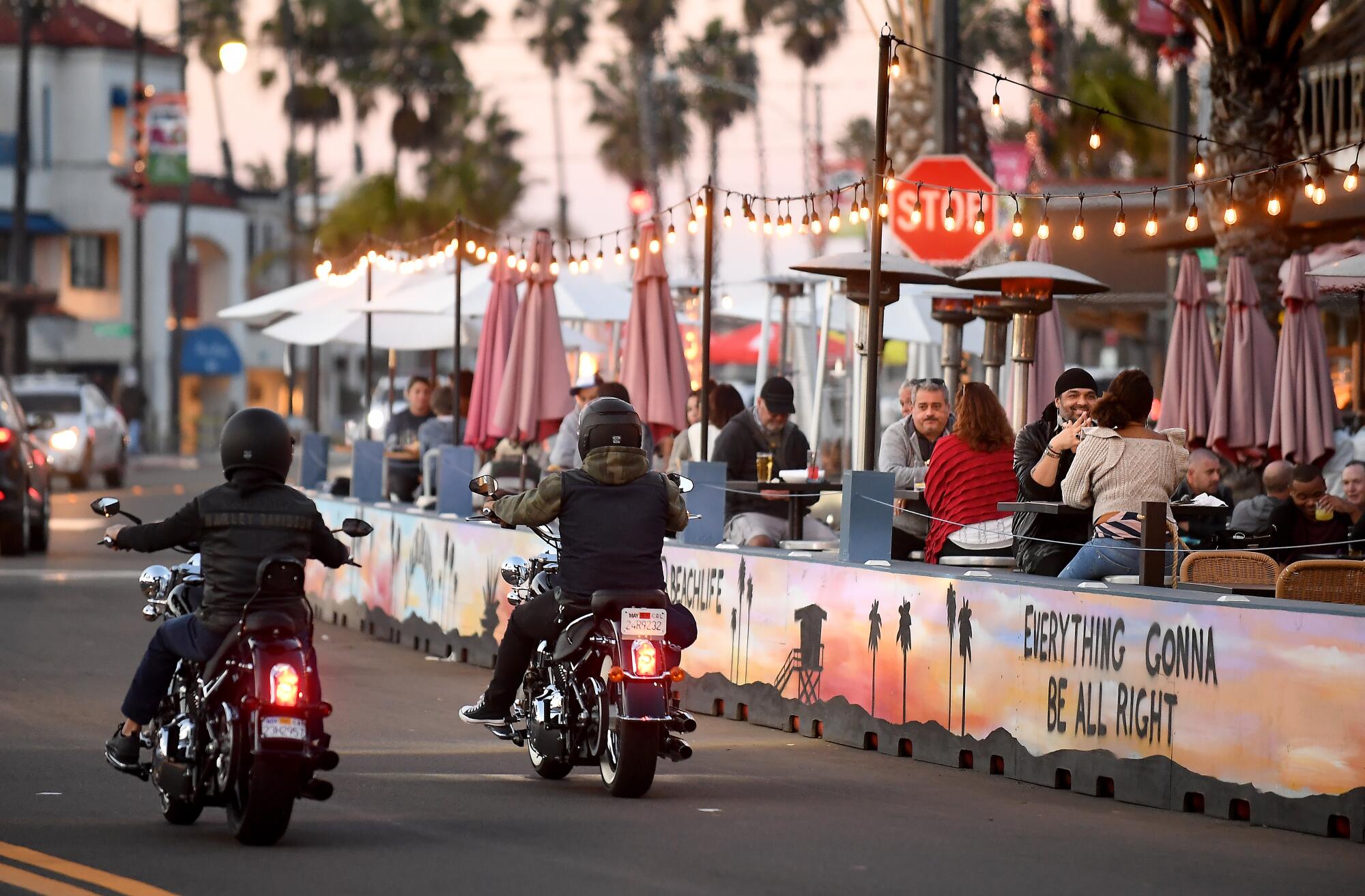 Two motorcyclists drive by as people dine alfresco at a restaurant in Redondo Beach. 