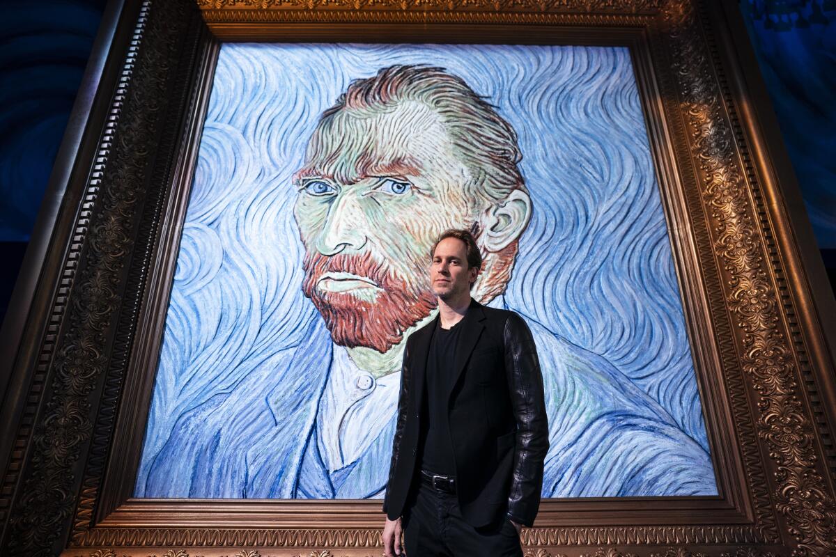 David Korins stands beside a giant replica of celebrated painter Vincent Van Gogh's self portrait at a preview of the Immersive Van Gogh exhibit at Pier 36, Friday, June 4, 2021, in New York. Korins has added a ceiling installation that uses almost 8,000 paint brushes to thrillingly reproduce “The Starry Night” and a station that uses artificial intelligence to give visitors an individualized letter from Van Gogh. (AP Photo/John Minchillo)