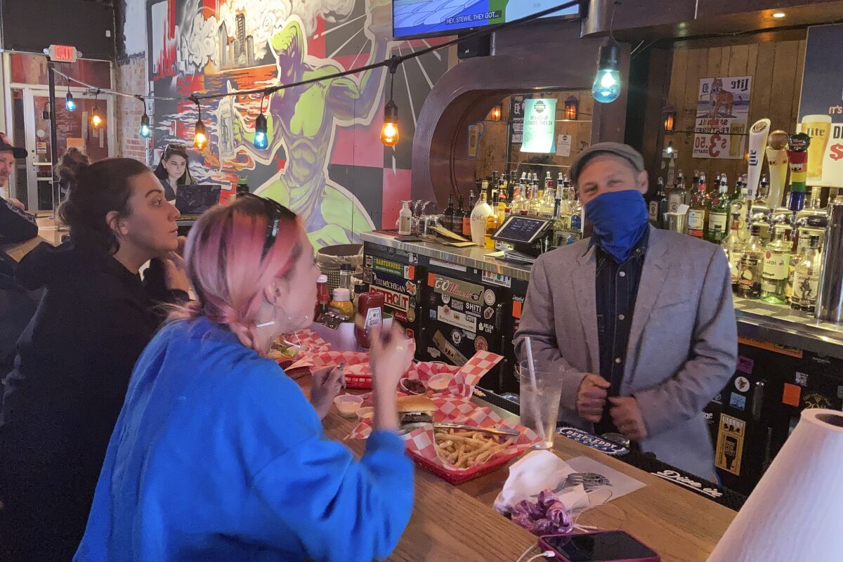 In a photo from May 6, 2021, Timothy Tharp with patrons Cecelia Shelley, center, and Amber Nolan, at his Checker Bar in downtown Detroit. Tharp also owns Grand Trunk Pub and the Whisky Parlor. He estimates that his businesses have lost about $1 million after closures caused by the coronavirus pandemic. But now as vaccinations increase and government-ordered lockdowns and restrictions to protect the public are being lifted, Tharpe believes the coronavirus pandemic could be remembered as just another hurdle the Motor City has had to leap. (AP Photo/Corey Williams)