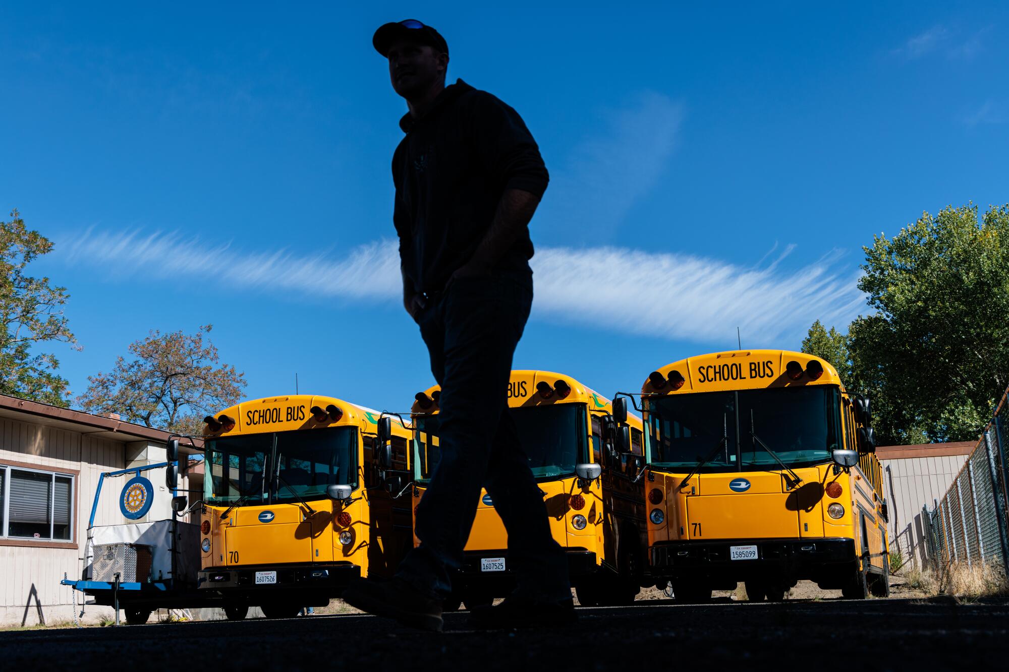 A man is silhouetted as he walks past a row of school buses.