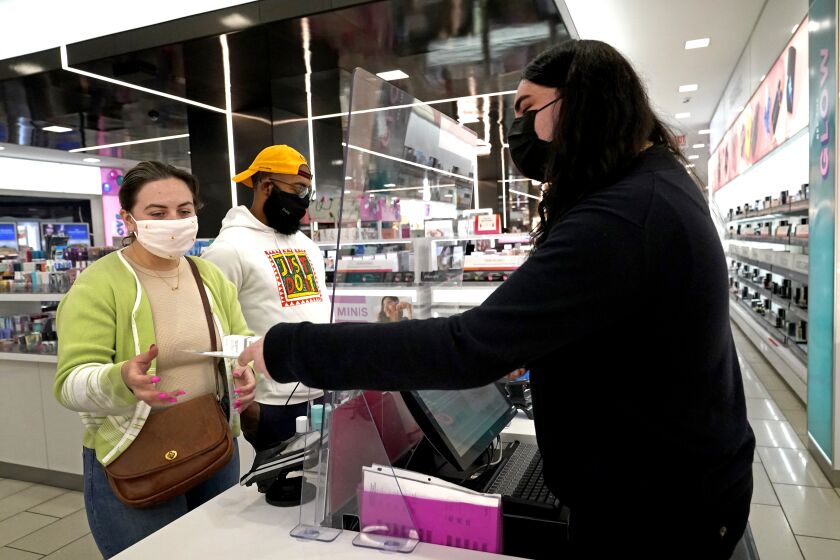 Cashier Druhan Parker, right, works behind a plexiglass shield Thursday, Nov. 19, 2020, as he checks out shoppers Cassie Howard, left, and Paris Black at an in Chicago. The accelerating surge of coronavirus cases across the U.S. is causing an existential crisis for America’s retailers and spooking their customers just as the critically important holiday shopping season nears. (AP Photo/Charles Rex Arbogast)
