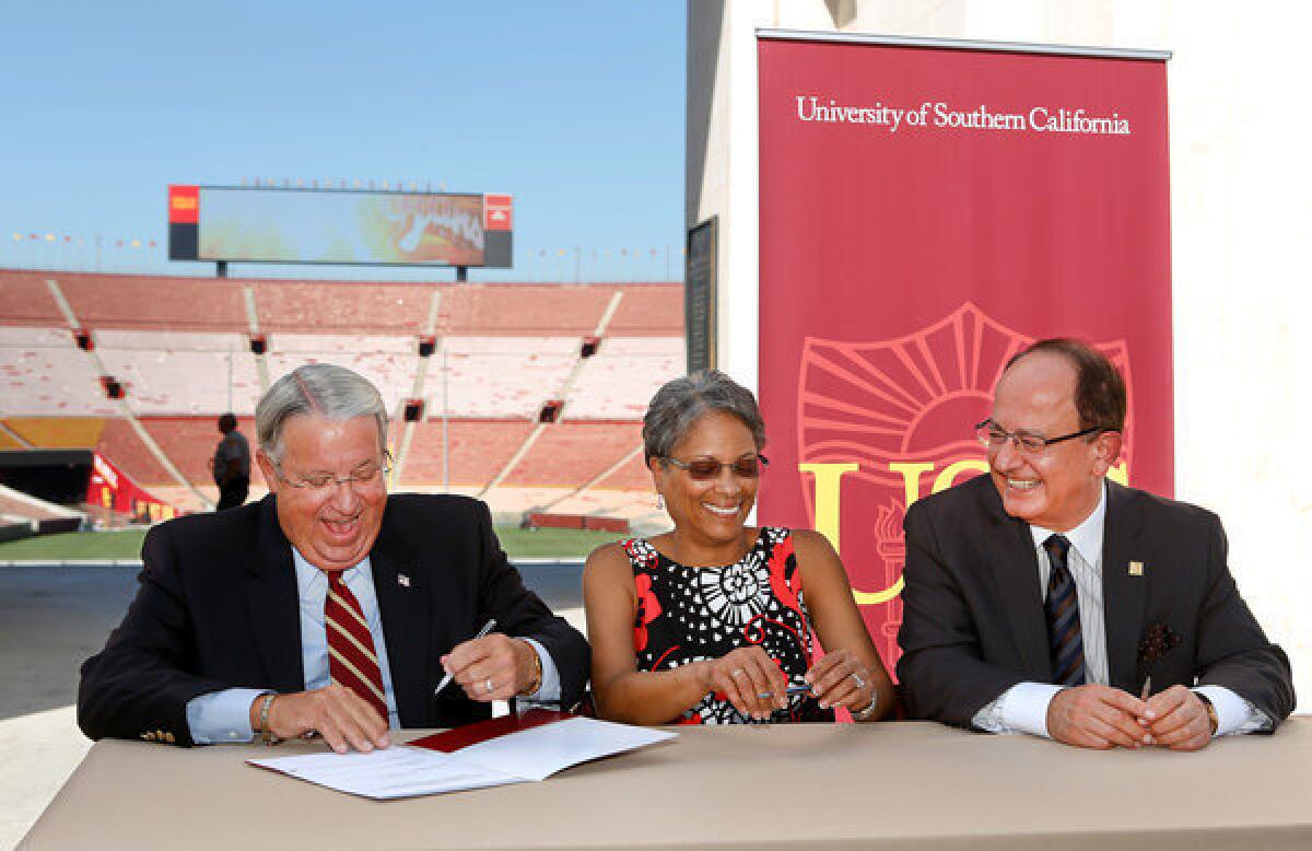 From left, Los Angeles County Supervisor Don Knabe, the president of the Coliseum Commission; Fabian Wesson, chair of the California Science Center board of directors; and USC President C.L. Max Nikias during a ceremonial signing of a lease giving USC control the Los Angeles Memorial Coliseum, seen in the background.