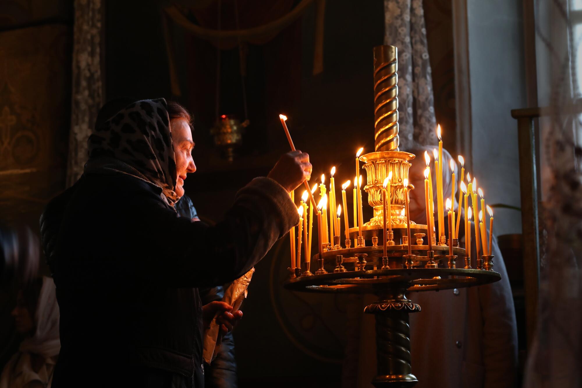 A woman adds a candle to a glowing display at church 