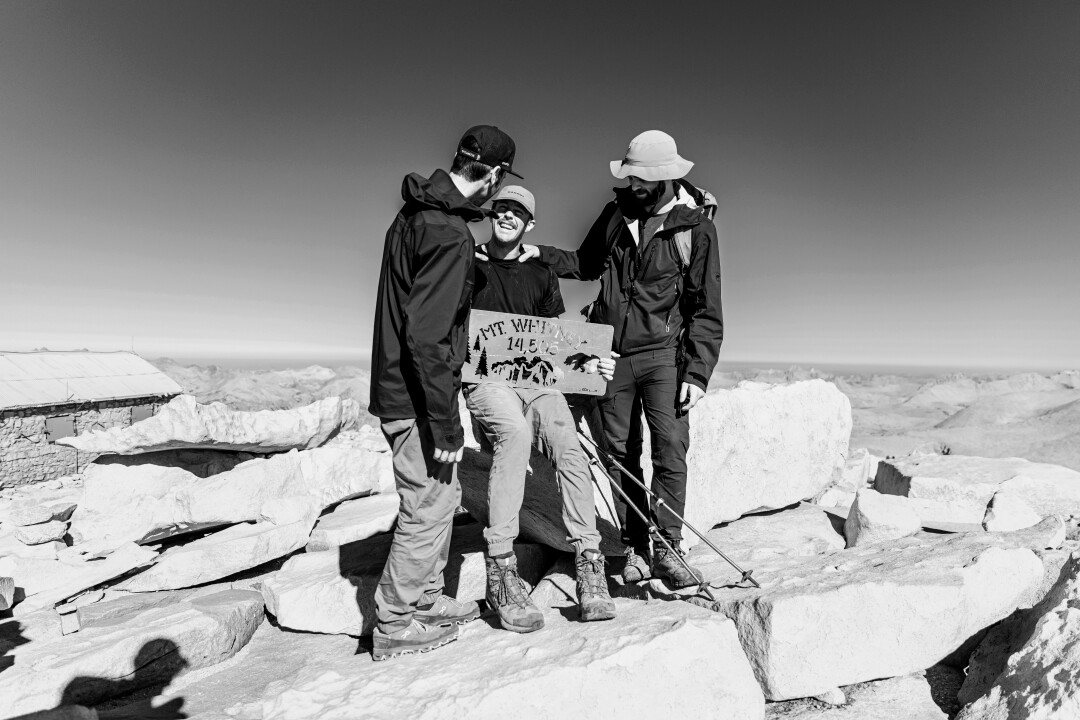 Three people atop Mt. Whitney, with the middle man holding a sign.