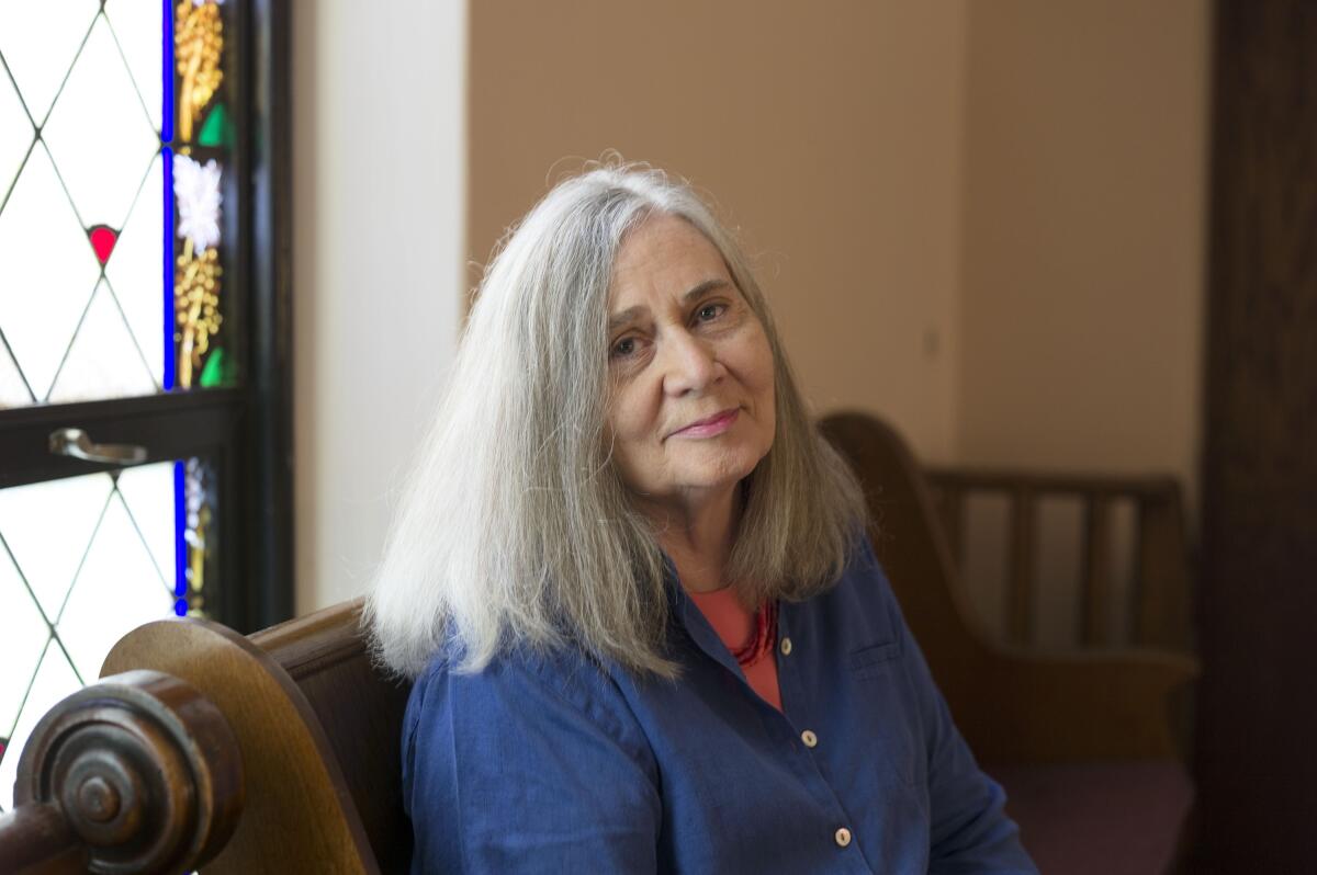 Marilynne Robinson sitting on a wood bench near a stained-glass window