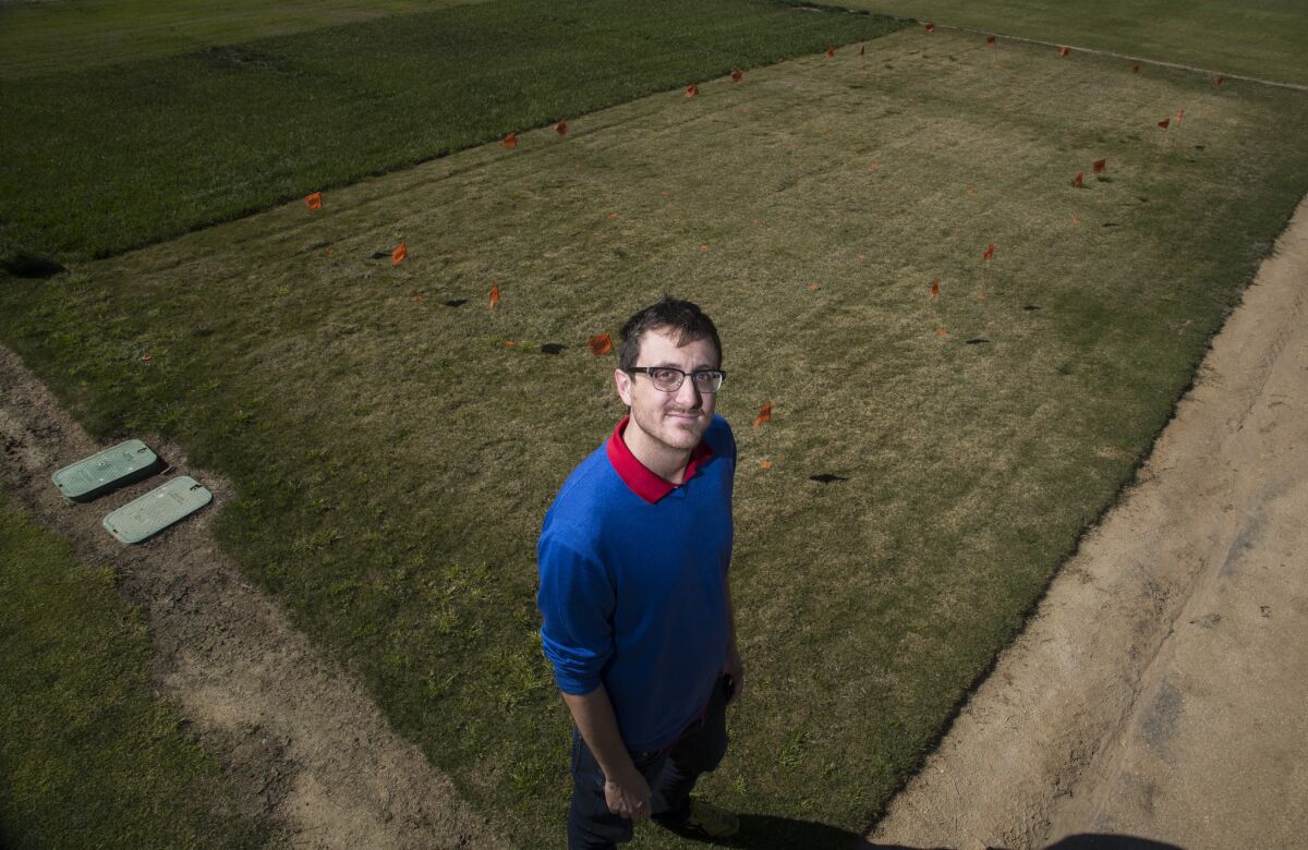 Marco Schiavon, a professional researcher at UC Riverside, stands on a large patch of Bermuda grass with tall fescue growing in the background.