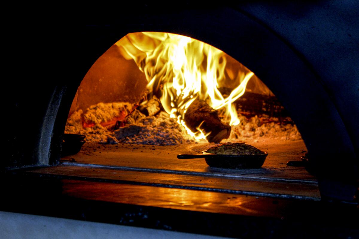 A skillet sits at the mouth of a wood-burning oven
