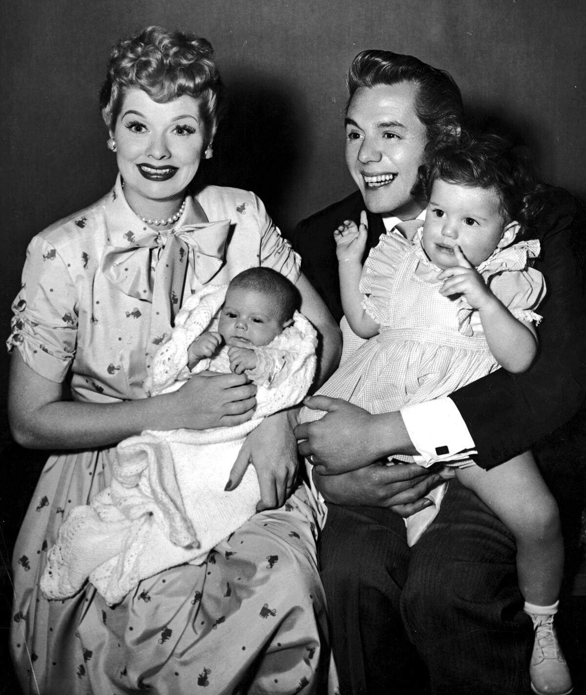 Lucille Ball and her husband, Desi Arnaz, laugh and smile while holding their two children, Desi Jr. and Lucie. 