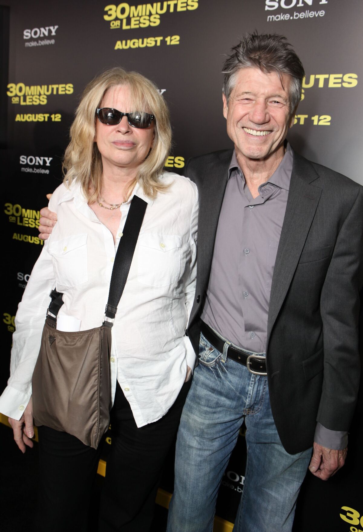 A woman in sunglasses stands with a smiling man at a movie premiere