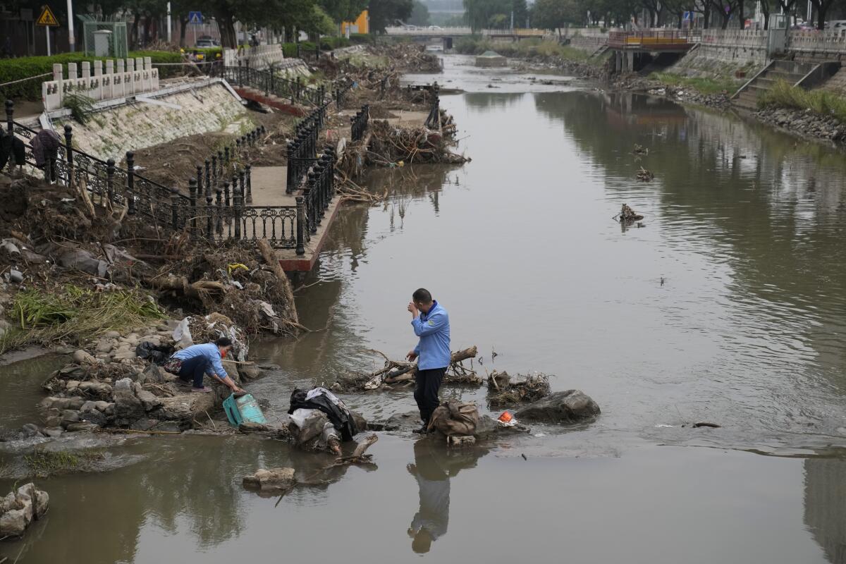 People on a damaged canal bank clogged with flood debris