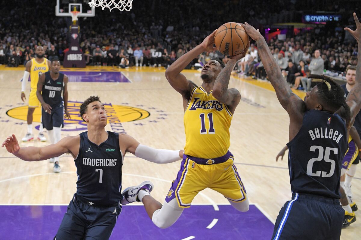 Lakers guard Malik Monk shoots as Dallas Mavericks forward Reggie Bullock and center Dwight Powell defend.