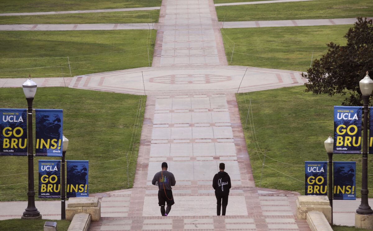 Two people walk through a pathway flanked by lawns and near signs that read "UCLA Go Bruins!"