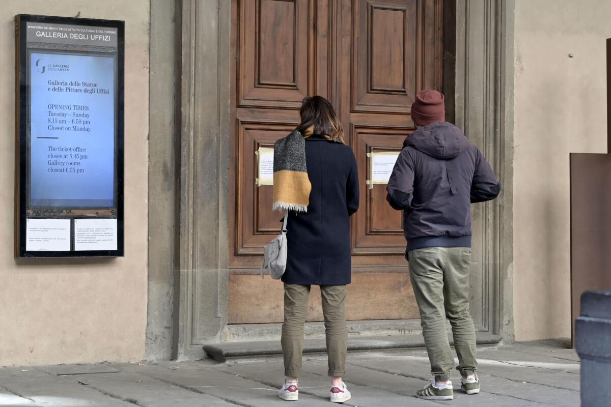 Two people look at a door to Italy's Uffizi, where a sign announcing its closure is posted.