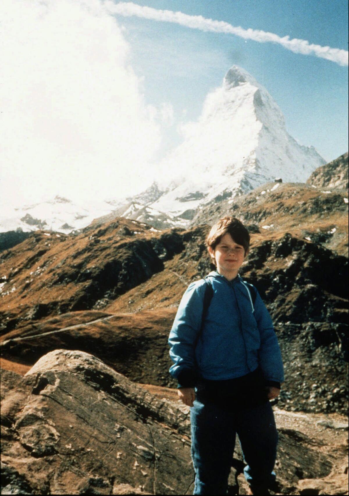 A young boy standing in front of a mountain.