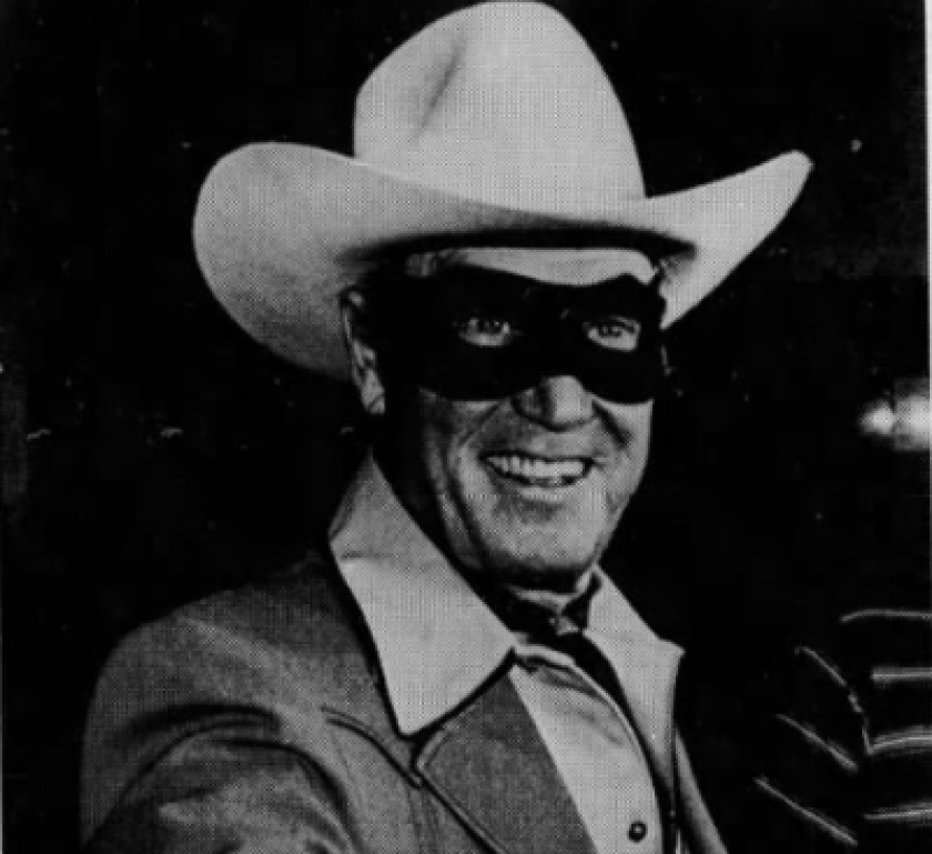 A man grins while wearing a black mask over his eyes and a white hat.