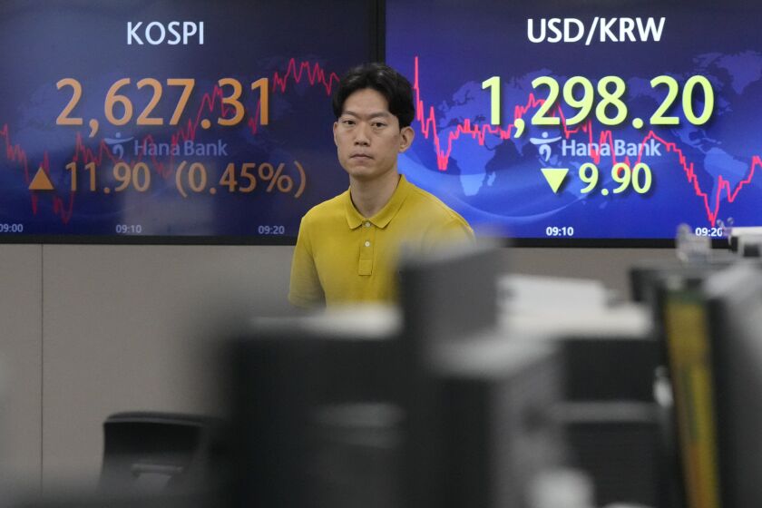 A currency trader walks by screens showing the Korea Composite Stock Price Index (KOSPI), top left, and the foreign exchange rate between U.S. dollar and South Korean won at the foreign exchange dealing room of the KEB Hana Bank headquarters in Seoul, South Korea, Wednesday, June 7, 2023. Asian shares were mixed Wednesday after a day of listless trading on Wall Street in the absence of market-moving data.(AP Photo/Ahn Young-joon)