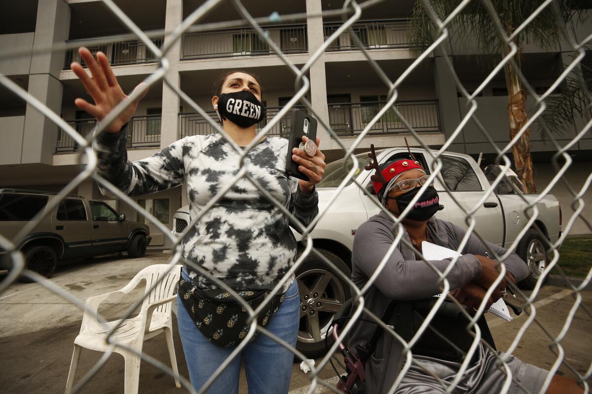 Two people in front of a building and behind a chain-link fence.