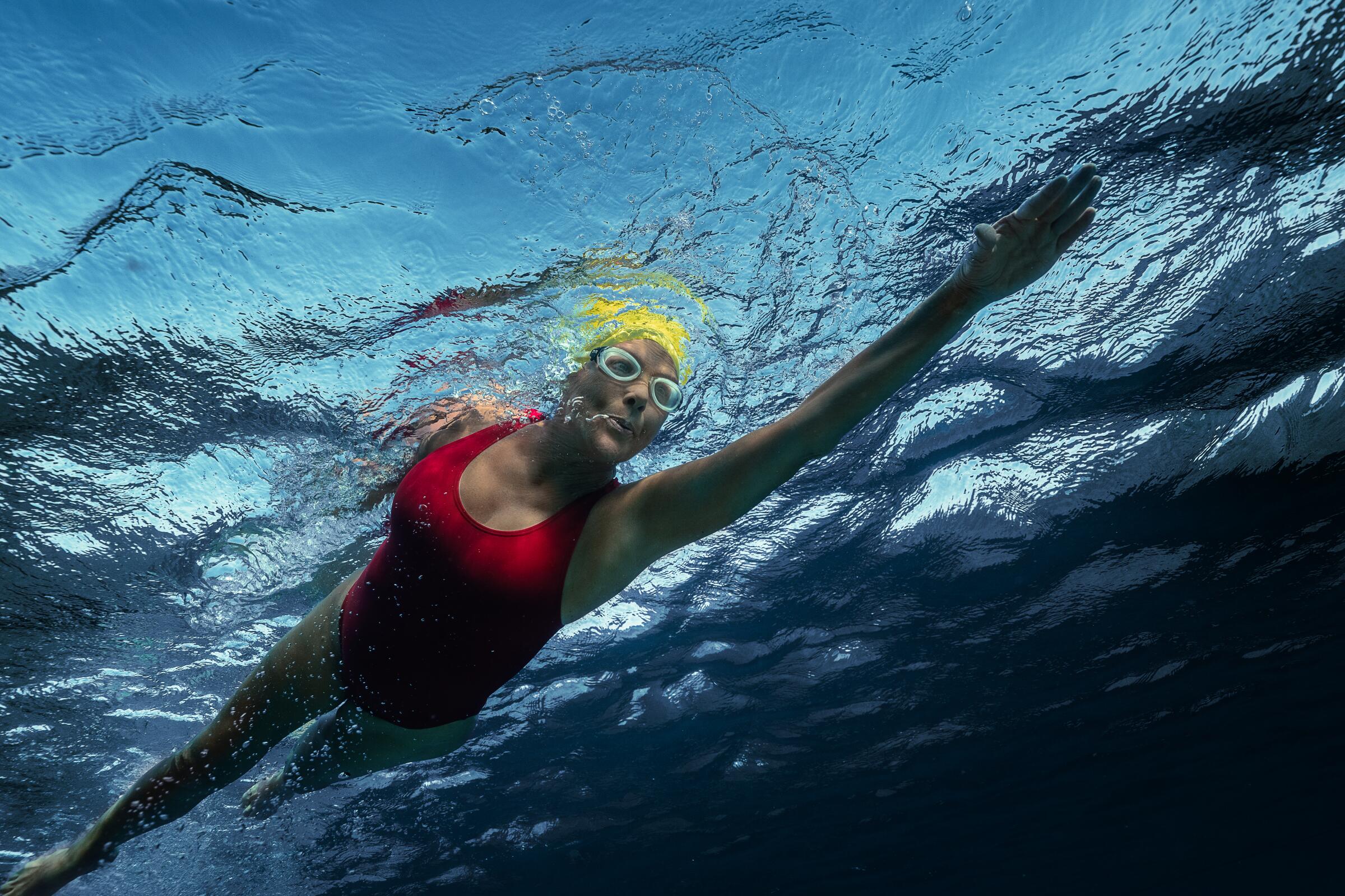 A female swimmer in red bathing suit and yellow cap, seen from underwater