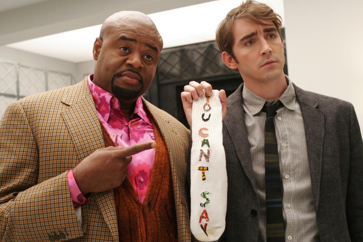 A man wearing a suit points at a sock that reads "you can't say" that's being held up by another man in a suit.